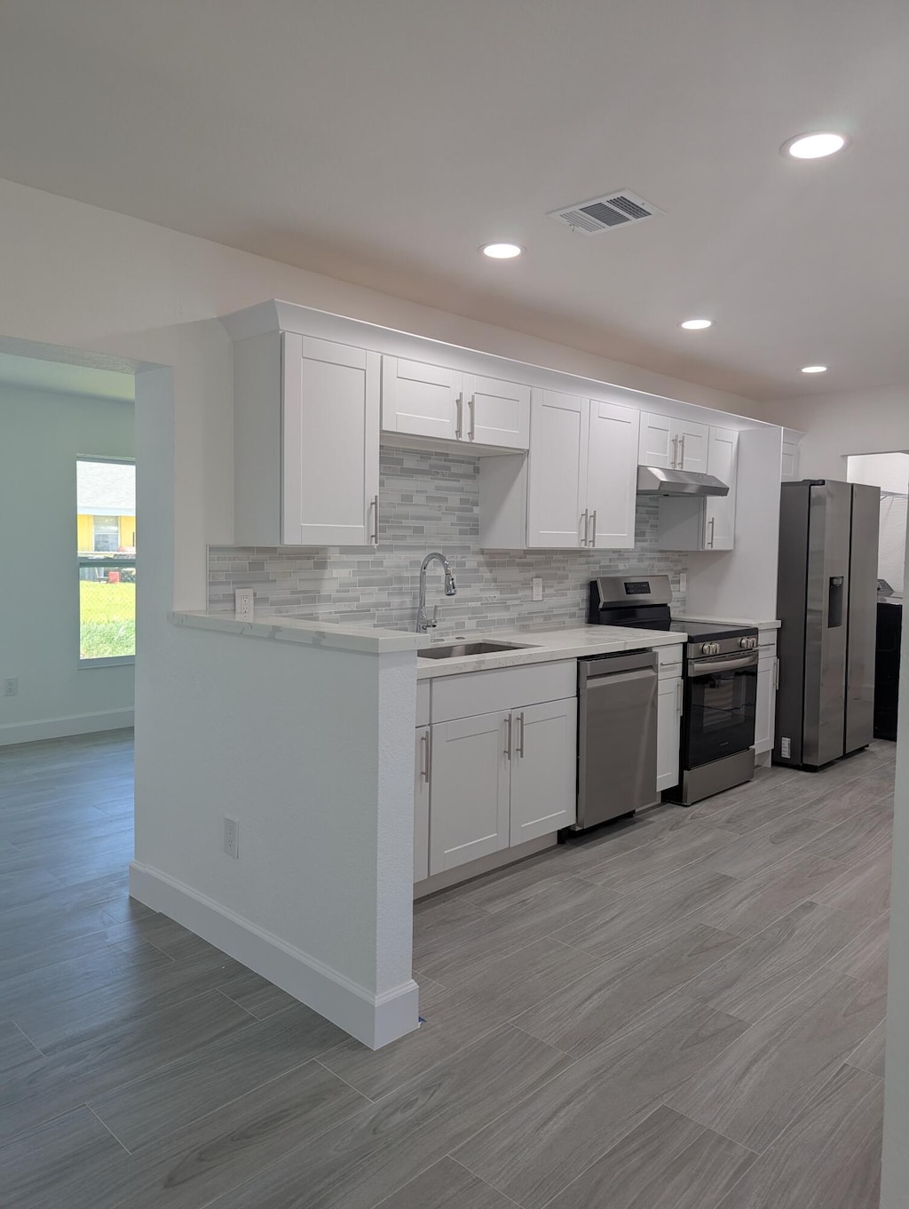 6830 2nd St, Limestone Creek, FL 33458 - kitchen featuring appliances with stainless steel finishes, light countertops, backsplash, white cabinetry, and under cabinet range hood