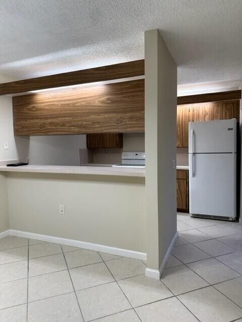 3310 33rd Way, West Palm Beach, FL 33407 - kitchen with white appliances, light tile patterned floors, a textured ceiling, light countertops, and brown cabinetry