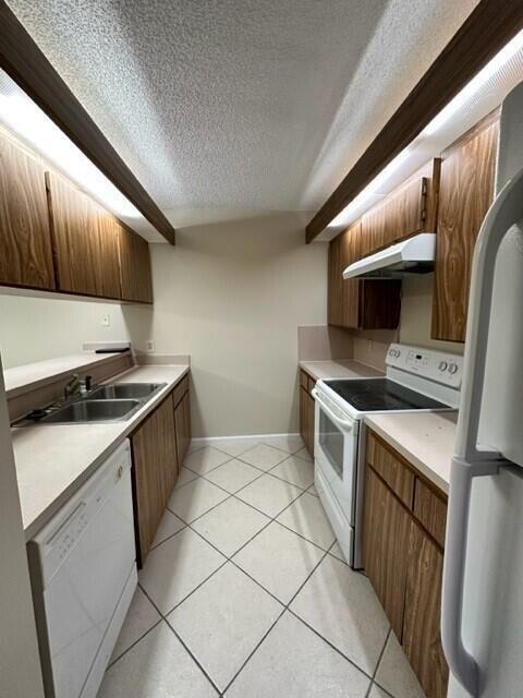 3310 33rd Way, West Palm Beach, FL 33407 - kitchen with white appliances, under cabinet range hood, a textured ceiling, light countertops, and light tile patterned floors