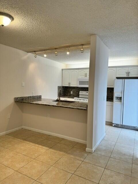 3822 38th Way, West Palm Beach, FL 33407 - kitchen with white appliances, decorative backsplash, light tile patterned flooring, a peninsula, and a textured ceiling