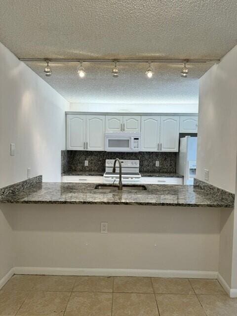 3822 38th Way, West Palm Beach, FL 33407 - kitchen featuring white appliances, a peninsula, rail lighting, dark stone counters, and a textured ceiling