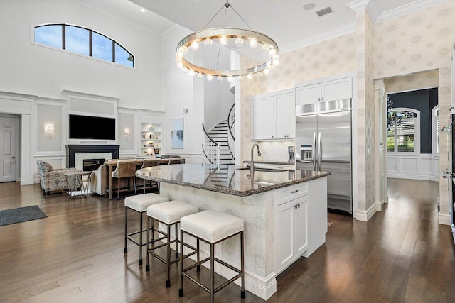 8199 Lost Creek Ln, Delray Beach, FL 33446 - kitchen featuring stainless steel built in fridge, a high ceiling, dark stone countertops, a fireplace, and white cabinets