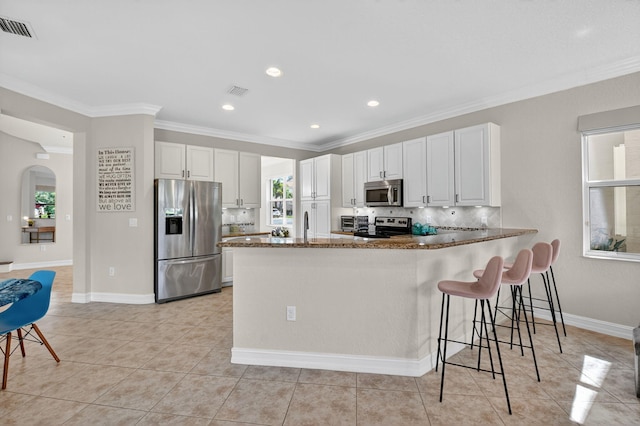 8110 Brigamar Isles Ave, Boynton Beach, FL 33473 - kitchen featuring appliances with stainless steel finishes, dark stone countertops, ornamental molding, white cabinets, and a peninsula