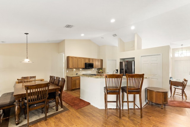 397 SW Jeanne Ave, Port Saint Lucie, FL 34953 - kitchen featuring stainless steel refrigerator with ice dispenser, black microwave, brown cabinets, wood finished floors, and high vaulted ceiling