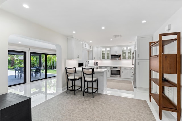 910 SW 21st St, Boca Raton, FL 33486 - kitchen featuring stainless steel appliances, a peninsula, light tile patterned floors, glass insert cabinets, and light countertops