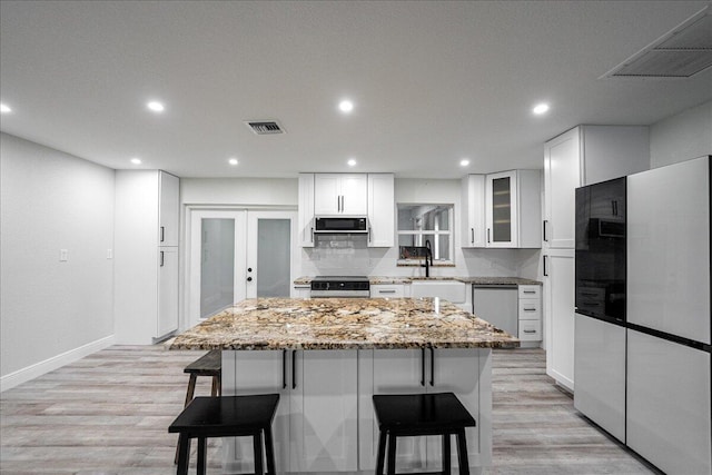 673 NE Horizon Ln, Port Saint Lucie, FL 34983 - kitchen featuring stainless steel appliances, a breakfast bar area, a center island, white cabinetry, and light stone counters