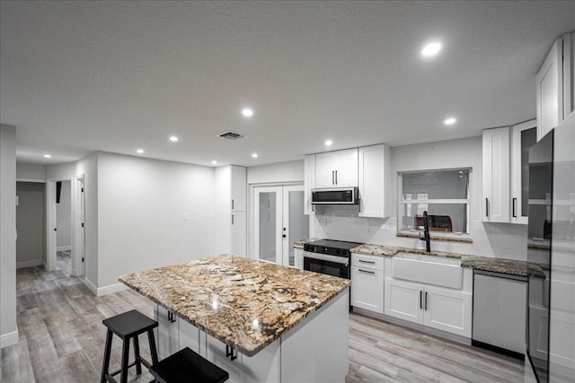 673 NE Horizon Ln, Port Saint Lucie, FL 34983 - kitchen featuring stainless steel appliances, a kitchen island, light stone counters, light wood finished floors, and recessed lighting