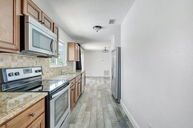 1669 SE N Blackwell Dr, Port Saint Lucie, FL 34952 - kitchen with stainless steel appliances, light wood-type flooring, decorative backsplash, light stone counters, and a textured ceiling