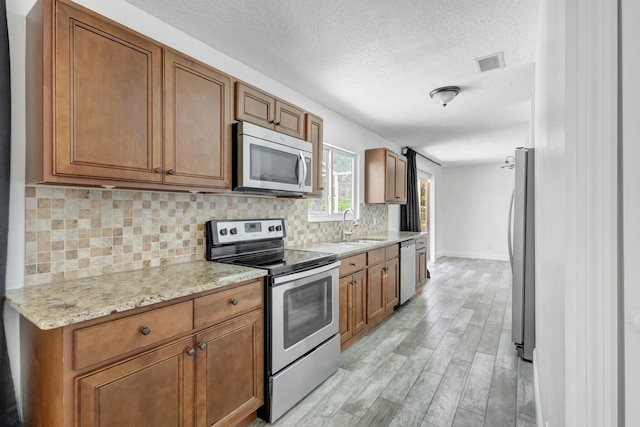 1669 SE N Blackwell Dr, Port Saint Lucie, FL 34952 - kitchen with appliances with stainless steel finishes, brown cabinets, light wood-style flooring, tasteful backsplash, and a textured ceiling