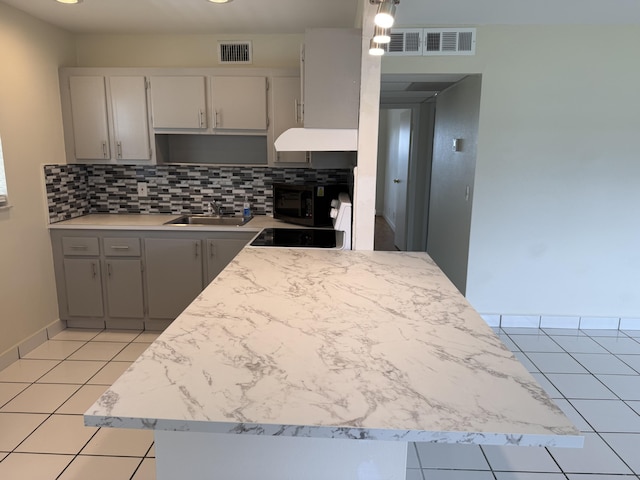 64 Waterford C, Delray Beach, FL 33446 - kitchen featuring tasteful backsplash, black microwave, light tile patterned floors, and custom range hood