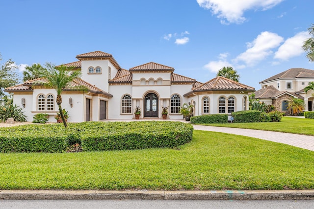 671 Indian River Dr, Melbourne, FL 32935 - mediterranean / spanish home with an attached garage, stucco siding, curved driveway, a front lawn, and french doors