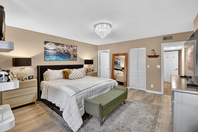 7270 Ashford Pl Unit 104, Delray Beach, FL 33446 - bedroom featuring light wood finished floors, a chandelier, a textured ceiling, and multiple closets