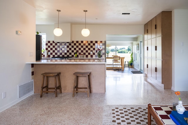 2931 SE Morningside Blvd, Port Saint Lucie, FL 34952 - kitchen featuring dark aggregate flooring, a peninsula, a breakfast bar area, tasteful backsplash, and hanging light fixtures