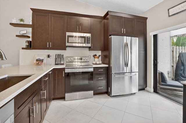 1005 NW 53rd St, Deerfield Beach, FL 33064 - kitchen with stainless steel appliances, open shelves, dark brown cabinetry, light stone countertops, and light tile patterned floors