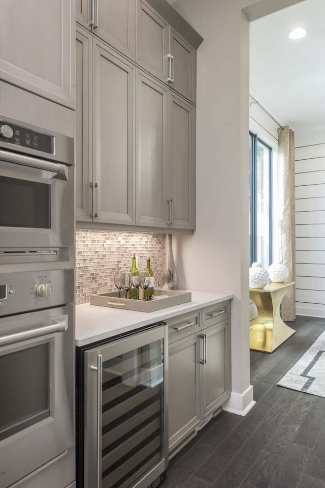 13405 Artisan Cir, Palm Beach Gardens, FL 33418 - indoor dry bar with beverage cooler, stainless steel double oven, backsplash, dark wood finished floors, and recessed lighting