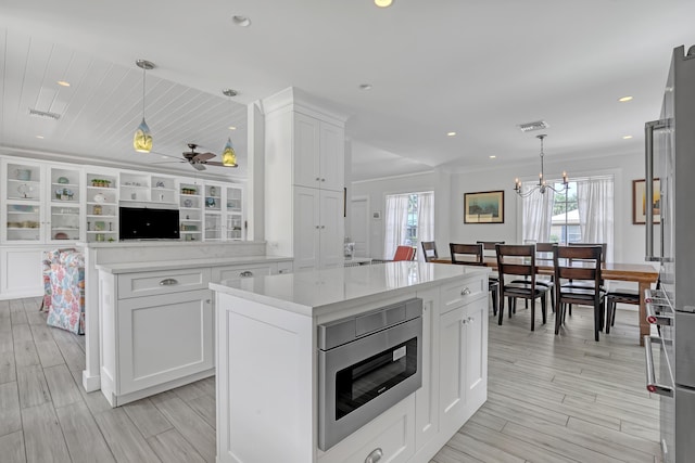 219 Claremont Ln, Palm Beach Shores, FL 33404 - kitchen featuring appliances with stainless steel finishes, white cabinets, a center island, decorative light fixtures, and light wood-style floors