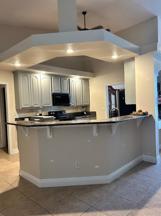 1701 SW Penrose Ave, Port Saint Lucie, FL 34953 - kitchen with black appliances, a kitchen breakfast bar, dark stone counters, light tile patterned flooring, and a peninsula