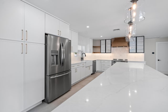77 Fairview E, Tequesta, FL 33469 - kitchen with appliances with stainless steel finishes, custom range hood, tasteful backsplash, white cabinetry, and light stone counters