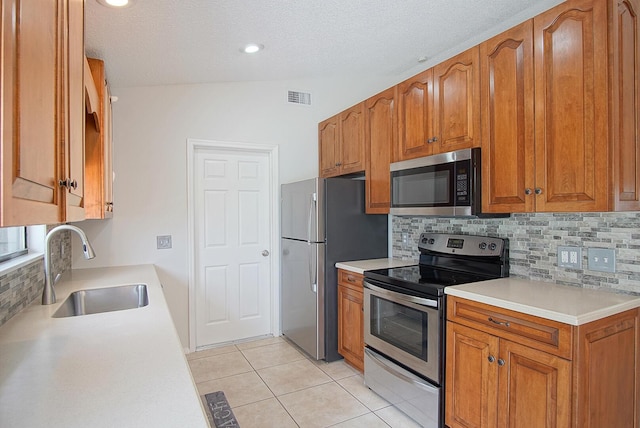 3126 SW Curcuma St, Port Saint Lucie, FL 34953 - kitchen with appliances with stainless steel finishes, tasteful backsplash, brown cabinetry, light countertops, and a textured ceiling