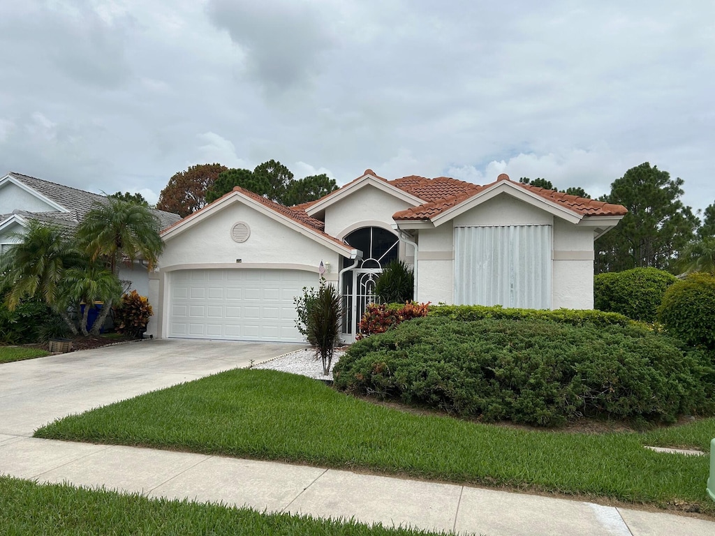 6995 SE Cutler Trl, Stuart, FL 34997 - view of front of house featuring an attached garage, driveway, stucco siding, a tile roof, and a front lawn