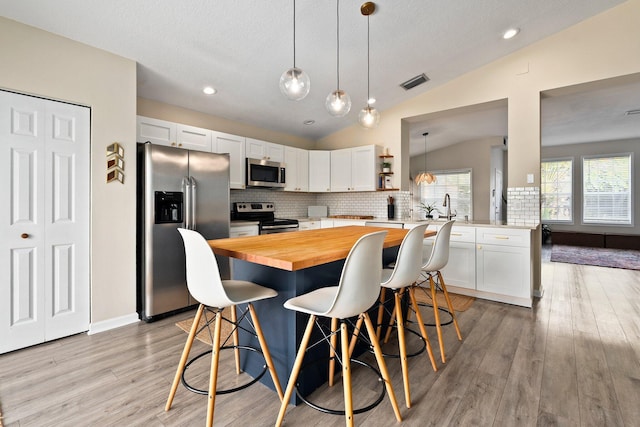 6351 Adams St, Jupiter, FL 33458 - kitchen featuring appliances with stainless steel finishes, wood counters, a kitchen breakfast bar, light wood-style floors, and decorative backsplash