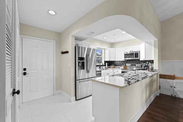 2950 SE Ocean Blvd Unit 119-6, Stuart, FL 34996 - kitchen featuring stainless steel appliances, a peninsula, light stone counters, white cabinets, and backsplash