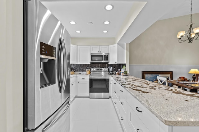 2950 SE Ocean Blvd Unit 119-6, Stuart, FL 34996 - kitchen with stainless steel appliances, wainscoting, a peninsula, white cabinetry, and light stone countertops