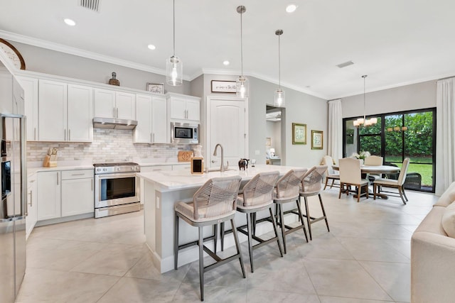 572 SE Villandry Way, Port Saint Lucie, FL 34984 - kitchen featuring appliances with stainless steel finishes, under cabinet range hood, tasteful backsplash, a breakfast bar area, and white cabinetry