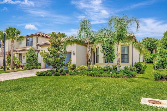 572 SE Villandry Way, Port Saint Lucie, FL 34984 - mediterranean / spanish-style house featuring decorative driveway, a front lawn, stucco siding, a tile roof, and a garage