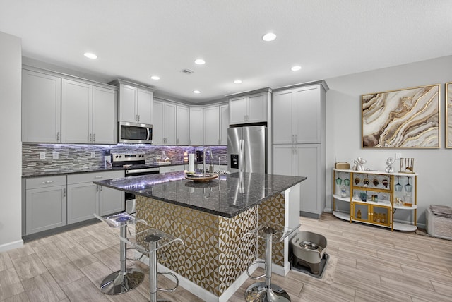 16360 Oakview Dr, Westlake, FL 33470 - kitchen with appliances with stainless steel finishes, gray cabinetry, a kitchen breakfast bar, backsplash, and light wood-style flooring