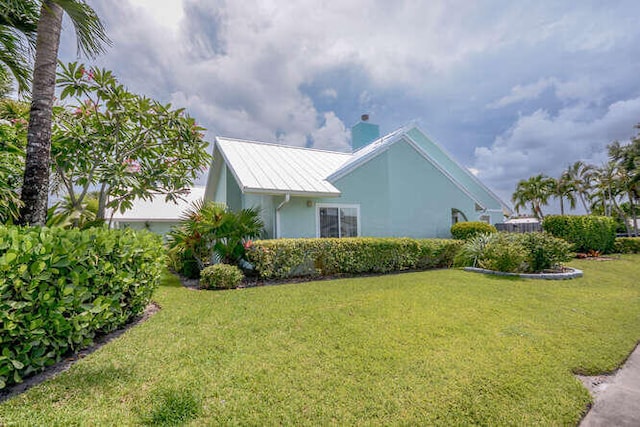 45 Birch Pl, Tequesta, FL 33469 - view of side of property with a lawn, stucco siding, a chimney, and a metal roof
