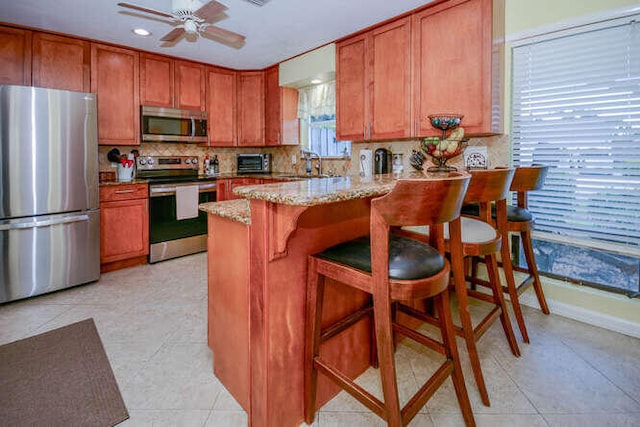 45 Birch Pl, Tequesta, FL 33469 - kitchen with appliances with stainless steel finishes, brown cabinetry, a peninsula, a ceiling fan, and tasteful backsplash