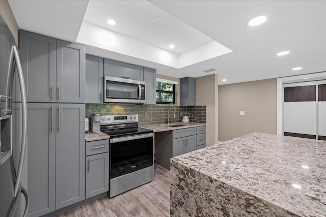 11863 Wimbledon Cir Unit 438, Wellington, FL 33414 - kitchen with appliances with stainless steel finishes, gray cabinetry, light wood-type flooring, light stone countertops, and backsplash