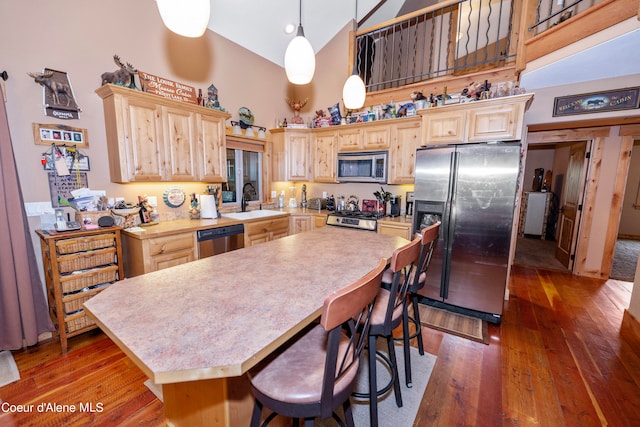 kitchen featuring a high ceiling, hanging light fixtures, appliances with stainless steel finishes, light brown cabinetry, and dark hardwood / wood-style flooring