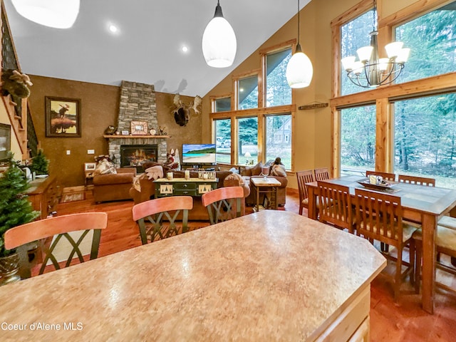 dining area with plenty of natural light, a stone fireplace, high vaulted ceiling, and an inviting chandelier