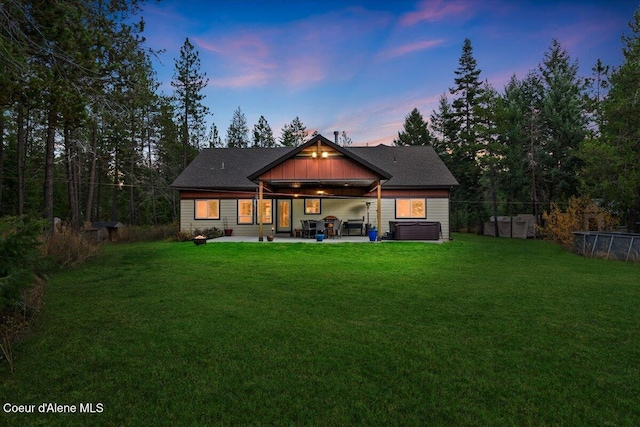 back house at dusk featuring a patio, a hot tub, central AC unit, and a lawn