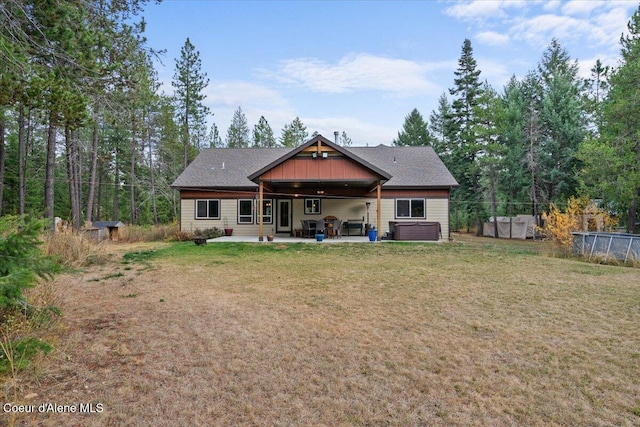 rear view of house with a hot tub, a patio area, and a lawn