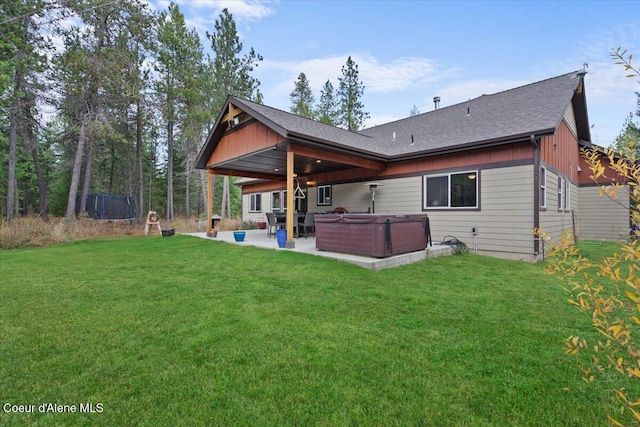 rear view of house featuring a yard, a trampoline, a hot tub, and a patio area