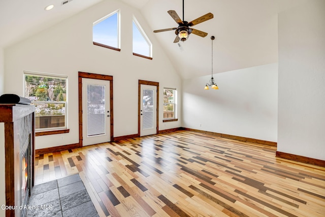 empty room with high vaulted ceiling, ceiling fan with notable chandelier, and light wood-type flooring