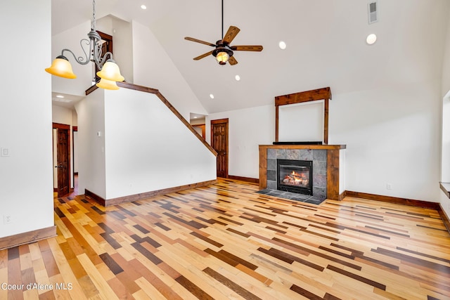 unfurnished living room featuring high vaulted ceiling, light hardwood / wood-style floors, ceiling fan with notable chandelier, and a fireplace