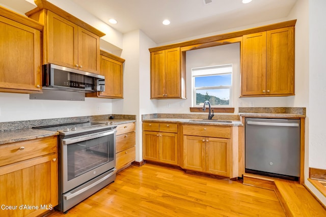 kitchen with light stone counters, sink, appliances with stainless steel finishes, and light hardwood / wood-style flooring