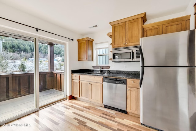 kitchen with plenty of natural light, stainless steel appliances, dark stone counters, and light hardwood / wood-style flooring