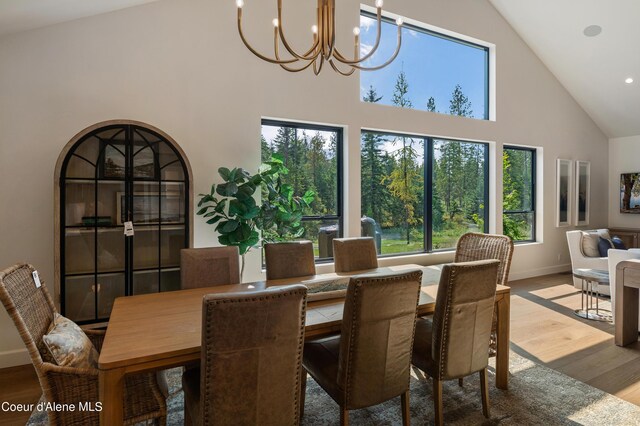 dining area with light wood-type flooring, high vaulted ceiling, and a chandelier