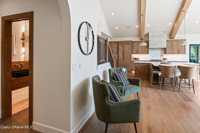 living room featuring lofted ceiling with beams, sink, and light hardwood / wood-style floors