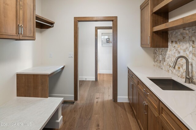 kitchen featuring dark wood-type flooring, light stone counters, sink, and backsplash