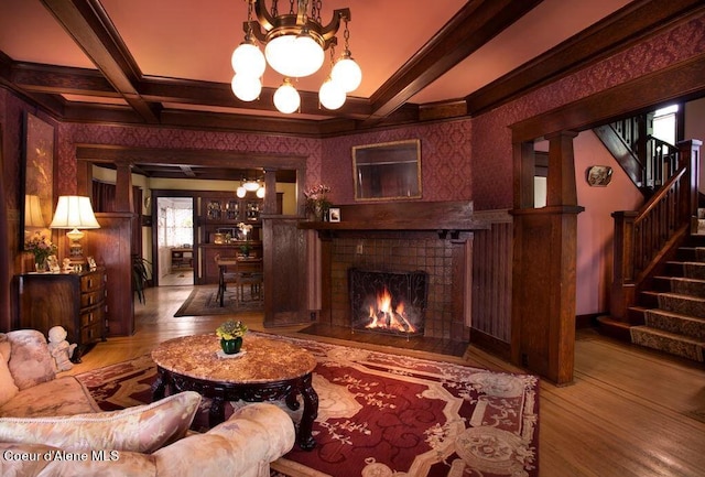 living room featuring hardwood / wood-style floors, coffered ceiling, an inviting chandelier, a brick fireplace, and beam ceiling