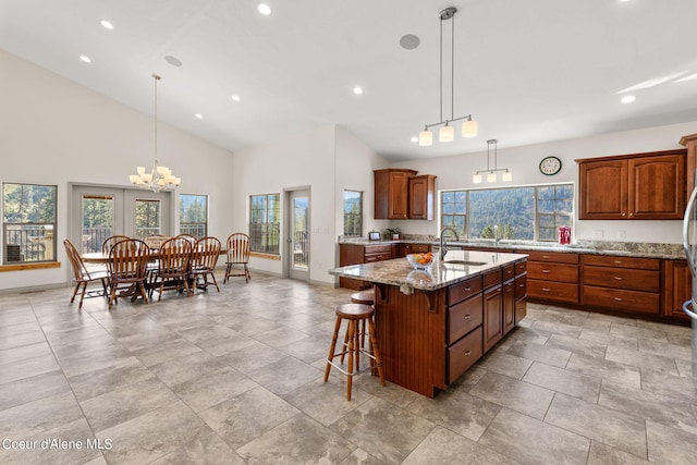 kitchen with pendant lighting, light stone countertops, a center island with sink, a breakfast bar area, and an inviting chandelier