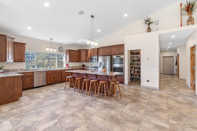 kitchen with a breakfast bar, a kitchen island with sink, stainless steel appliances, and light stone counters