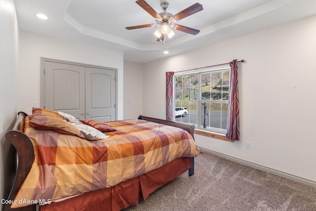 bedroom with a closet, ceiling fan, dark carpet, and a raised ceiling