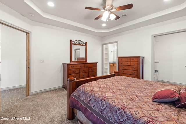 bedroom with light carpet, ensuite bath, ceiling fan, and a raised ceiling